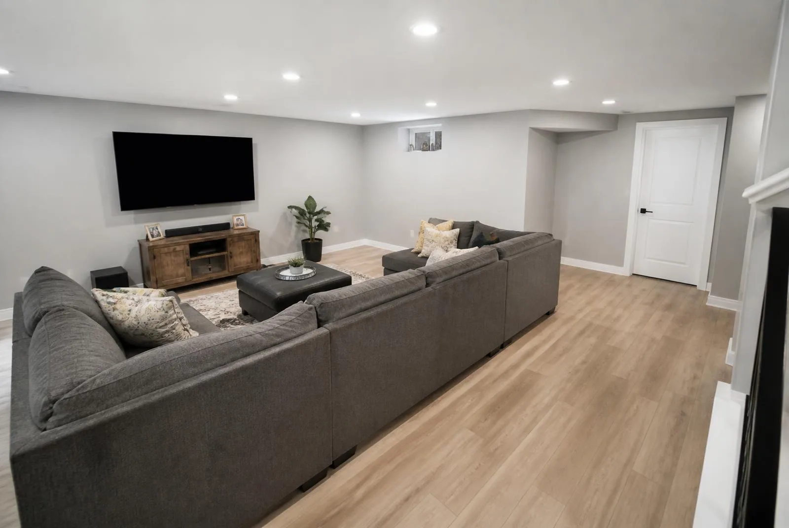 Finished basement family lounge with sectional sofa, wall-mounted TV, and vinyl plank flooring